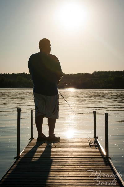 A man fishing off of a dock in the late afternoon