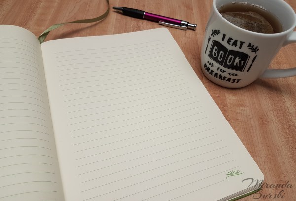 An open notebook, pen, and cup of tea