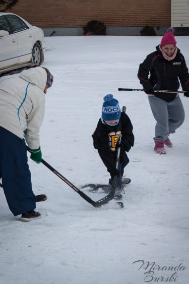 A young kid and two adults playing street hockey