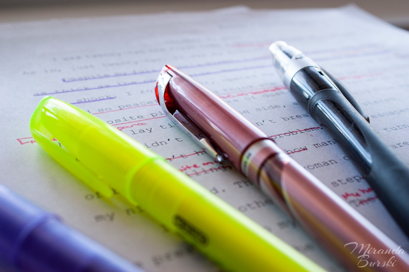 A pencil, red pen, yellow highlighter, and blue highlighter lying on marked-up text.