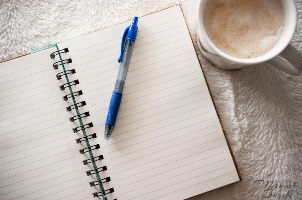 A pen sitting on top of a blank notebook page, with a cafe-mocha beside it.