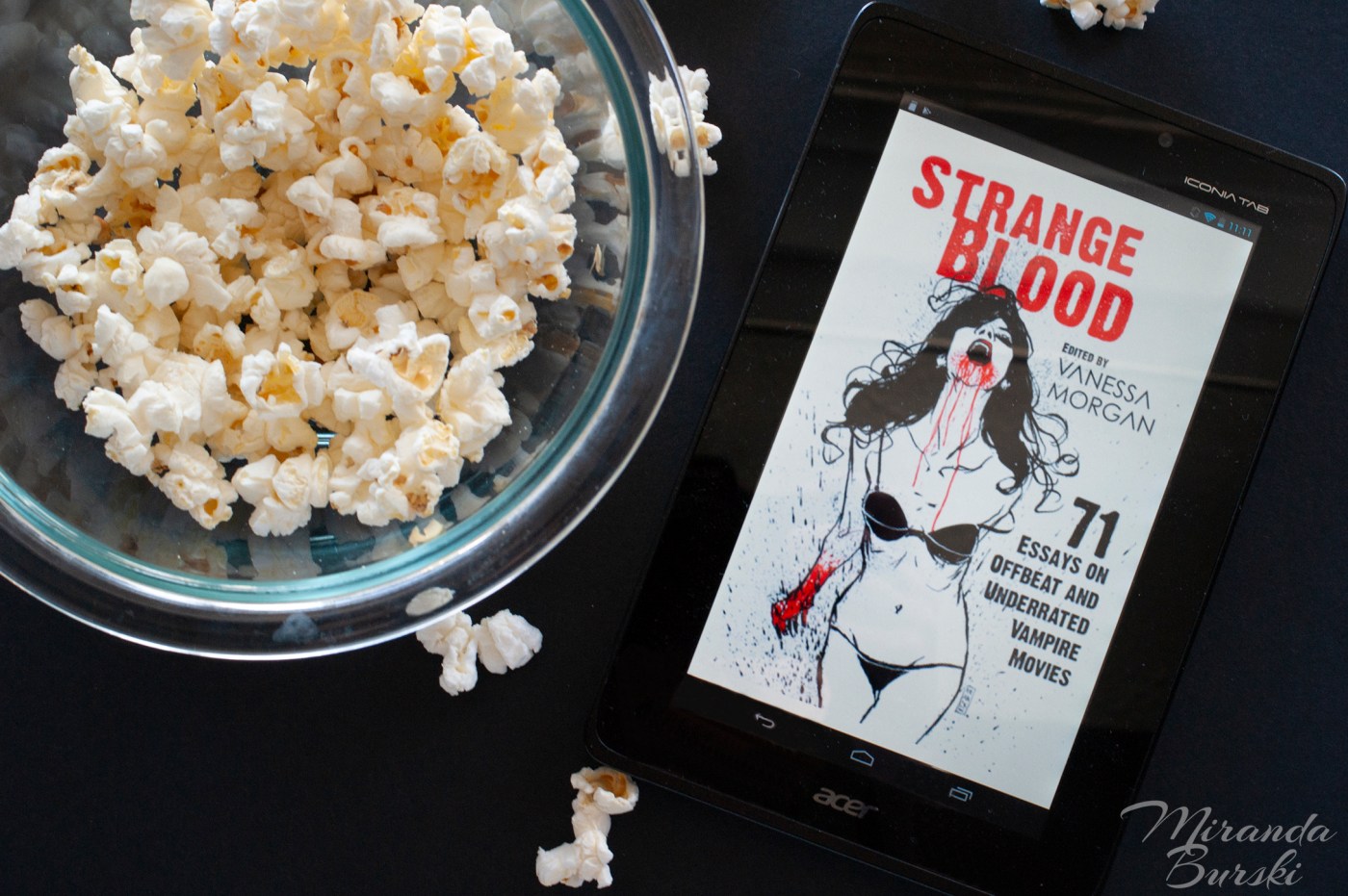 An e-book copy of Strange Blood, edited by Vanessa Morgan, beside a bowl of popcorn.