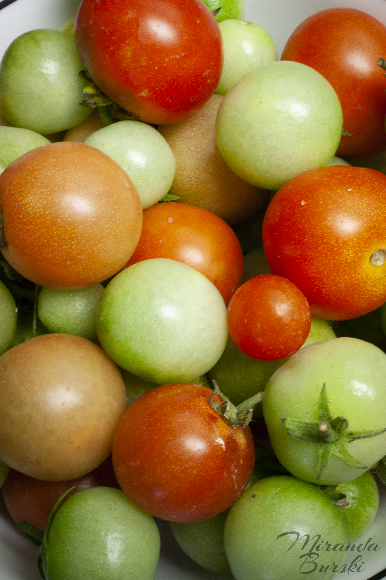 A bowl of green, orange and red cherry tomatoes.