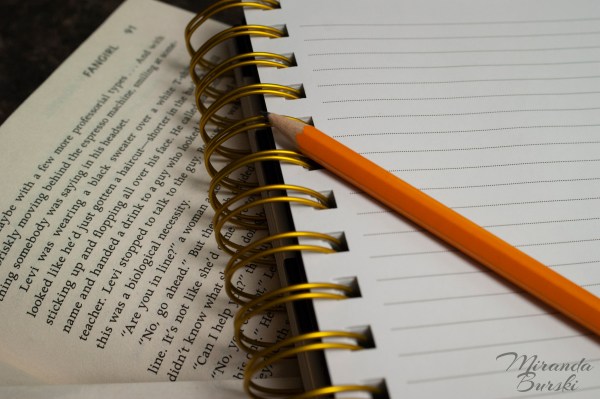 A pencil and notebook on top of an open copy of Fangirl, by Rainbow Rowell