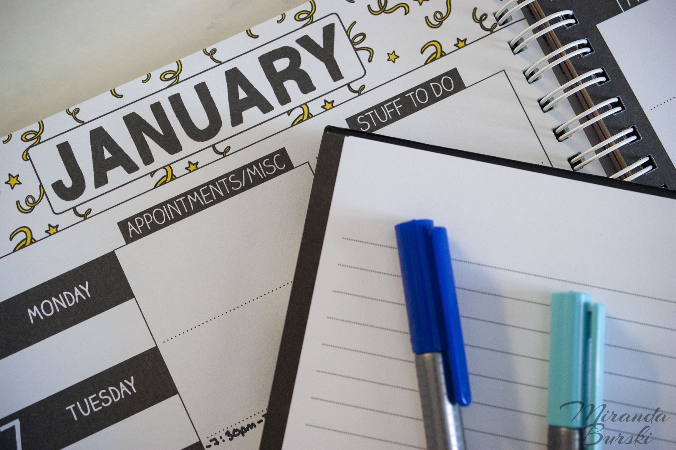 Blue markers on top of an empty notebook and January weekly planner.