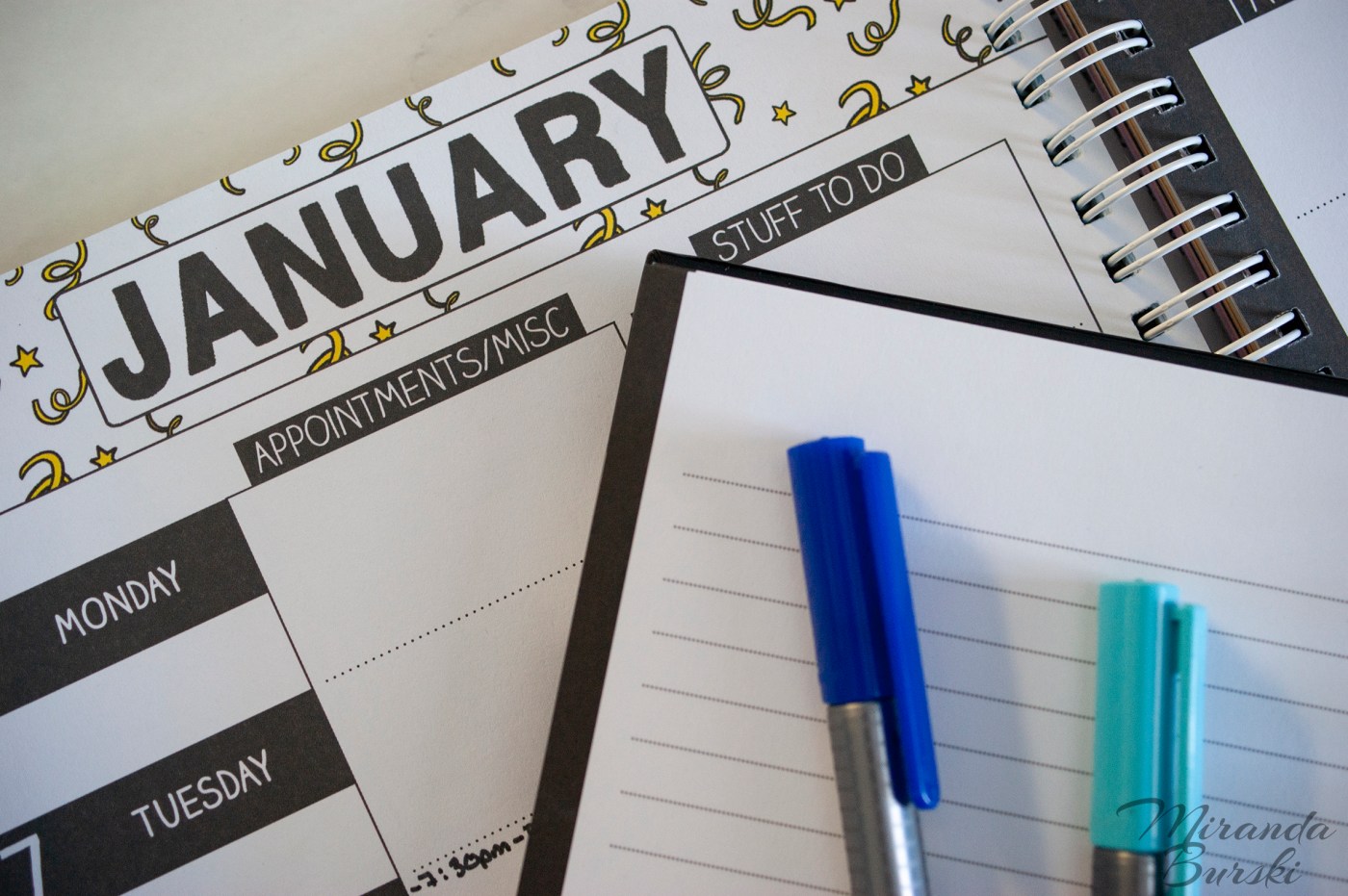 Blue markers on top of an empty notebook and January weekly planner.