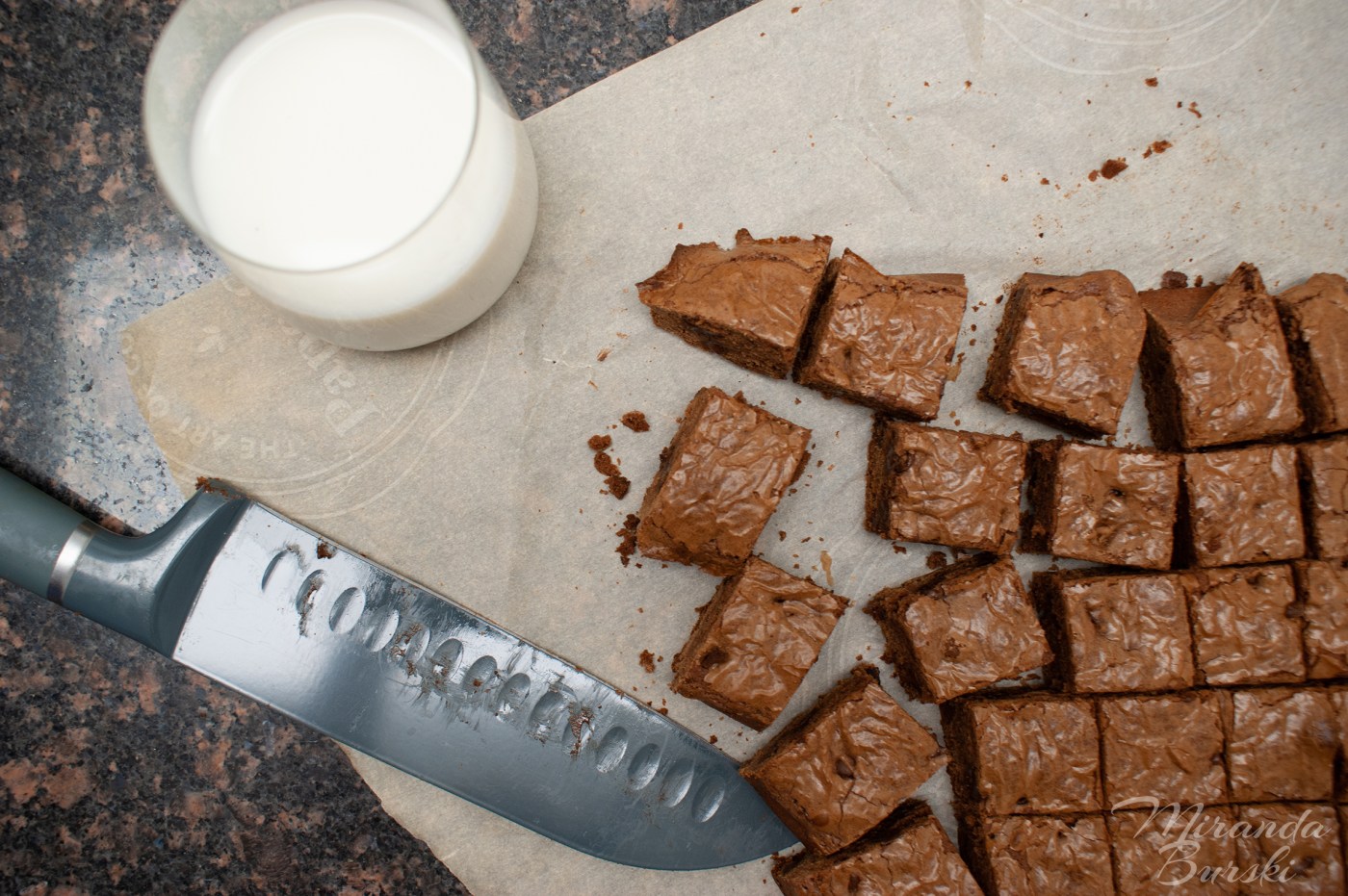 Brownies next to a knife and glass of milk.