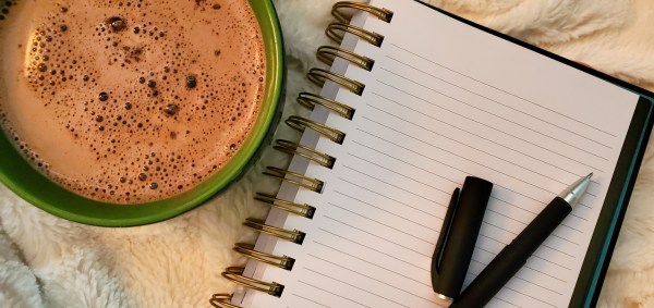 A cup of hot chocolate beside a notebook and pen
