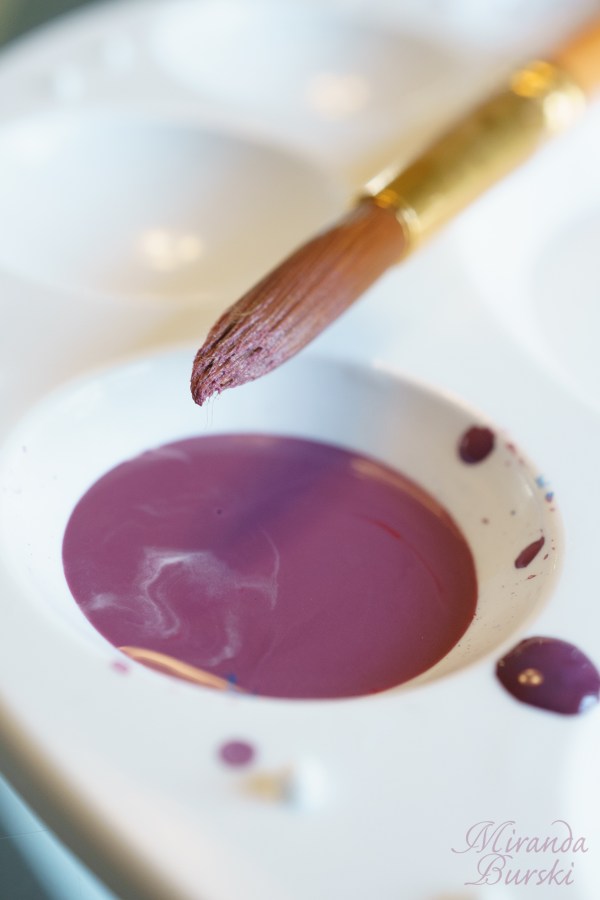 A paintbrush that has been dipped in purple watercolour paint, sitting on a palette.